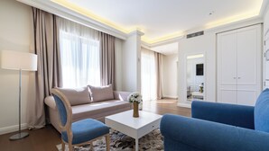 A modern hotel room with a sofa, a blue armchair, a white coffee table, and a large wardrobe. - Hotel Eden (Budva)