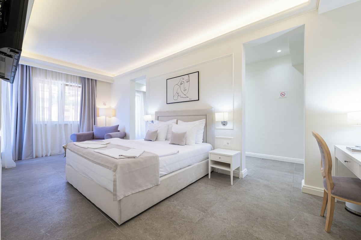 A hotel room with a large bed, a desk, a chair, a nightstand, and a wall-mounted artwork.