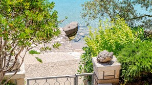 Blick auf die Küste mit einem Steinweg, der zum Wasser führt, umgeben von Grünpflanzen und einer Brüstung.