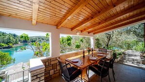 Un comedor con mesa y sillas de madera, vista a un lago y una pared de piedra.