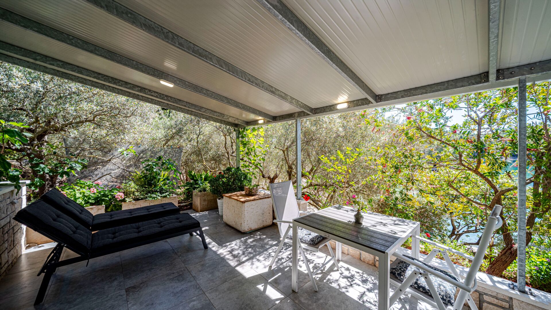 An outdoor patio with a black sofa, a wooden table, and potted plants.