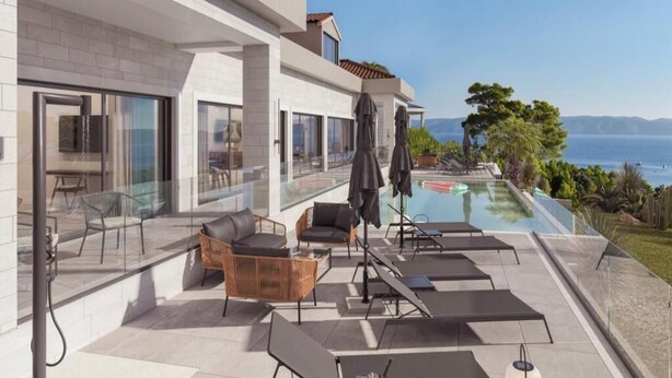 Un espace piscine extérieur moderne, doté de chaises longues, d’un coin repas et offrant une vue sur la mer.