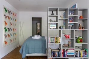 Ein Schlafzimmer mit einem Bett, einem Bücherregal und einer Wand mit farbenfrohen Pferdeabbildungen.
