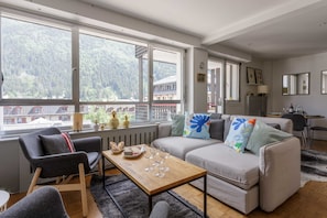 Ein modernes Wohnzimmer mit einer Couch, Sesseln, einem Couchtisch und großen Fenstern mit Blick auf ein bewaldetes Gebiet.