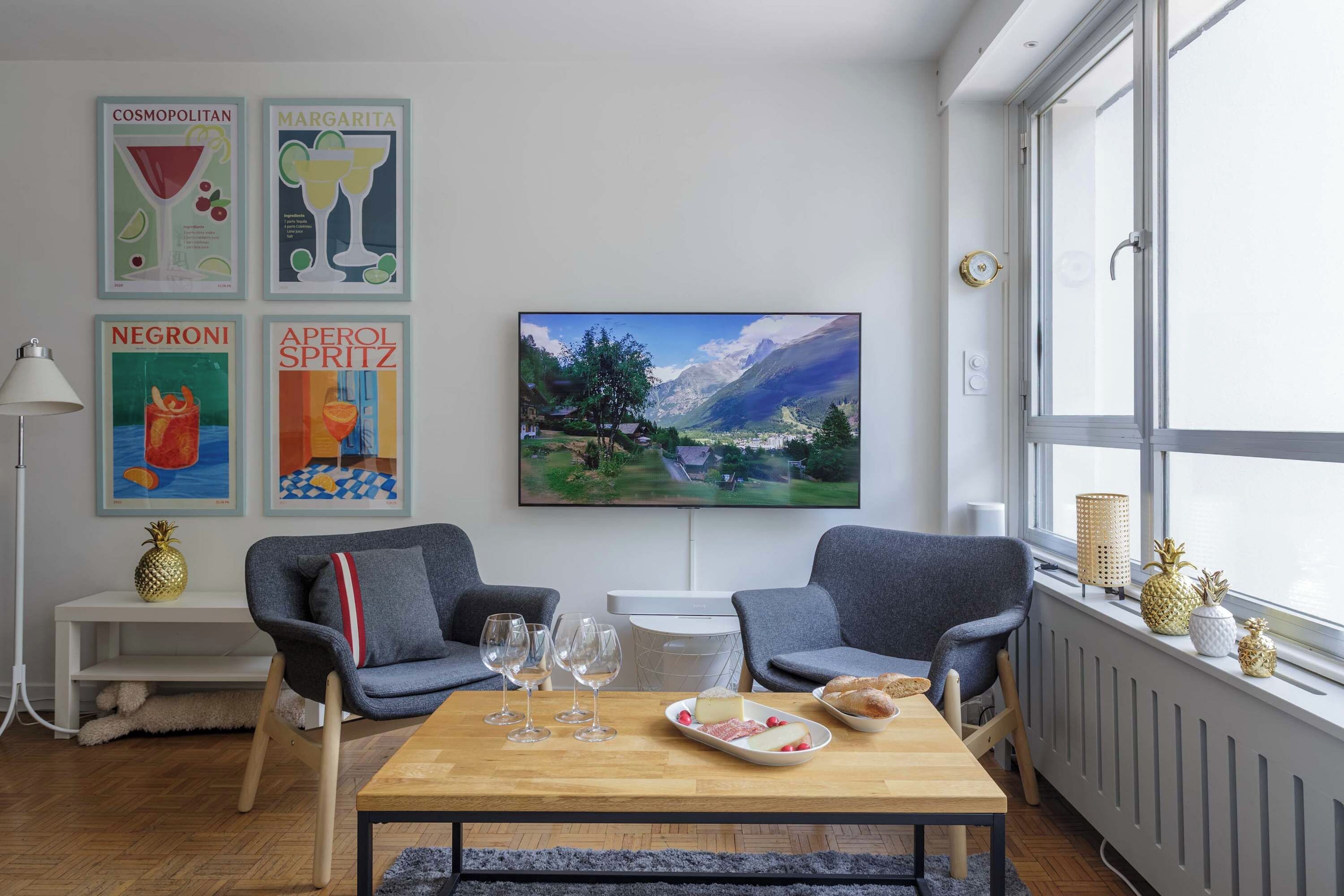 A modern living room with two grey armchairs, a wooden coffee table, and a large window with a view of a mountain landscape.