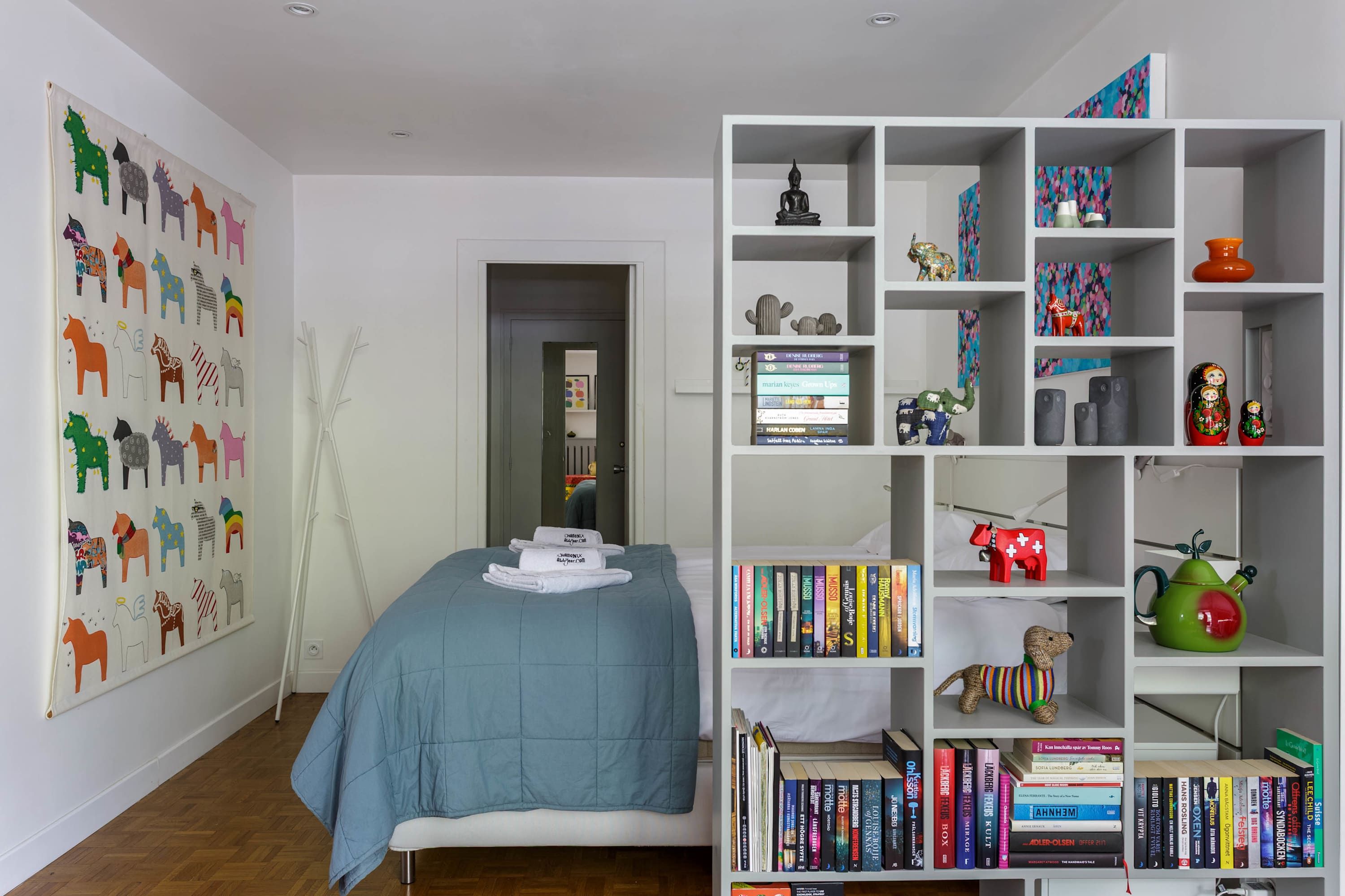 Quarto com cama, estante de livros e parede decorada com ilustrações de animais.