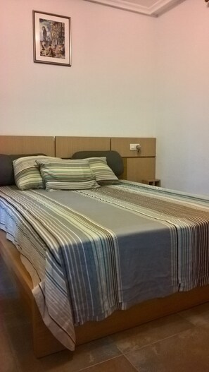 Ein Schlafzimmer mit einem Bett, Kissen, einem Nachttisch und einem gerahmten Bild an der Wand.