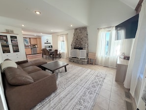 A living room with a sofa, a dining table, a stone fireplace, and a kitchen in the background.