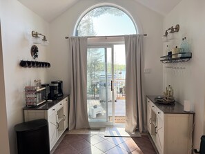A kitchen with a coffee maker, a sink, a countertop, and a view of the outdoors through a glass door.