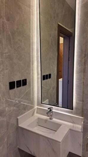 A bathroom with a marble sink, a large mirror, and a door in the background. - Casa Residence Al Narjees (Riyadh, Al Narjis neighborhood)