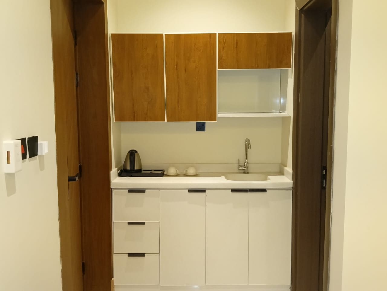 A compact kitchen with white cabinets, a sink, and a kettle.