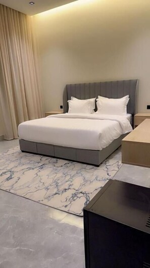 A modern hotel room with a large bed, a bedside table, a flat-screen TV, and a marble-patterned rug. - Casa Residence Al Narjees (Riyadh, Al Narjis neighborhood)
