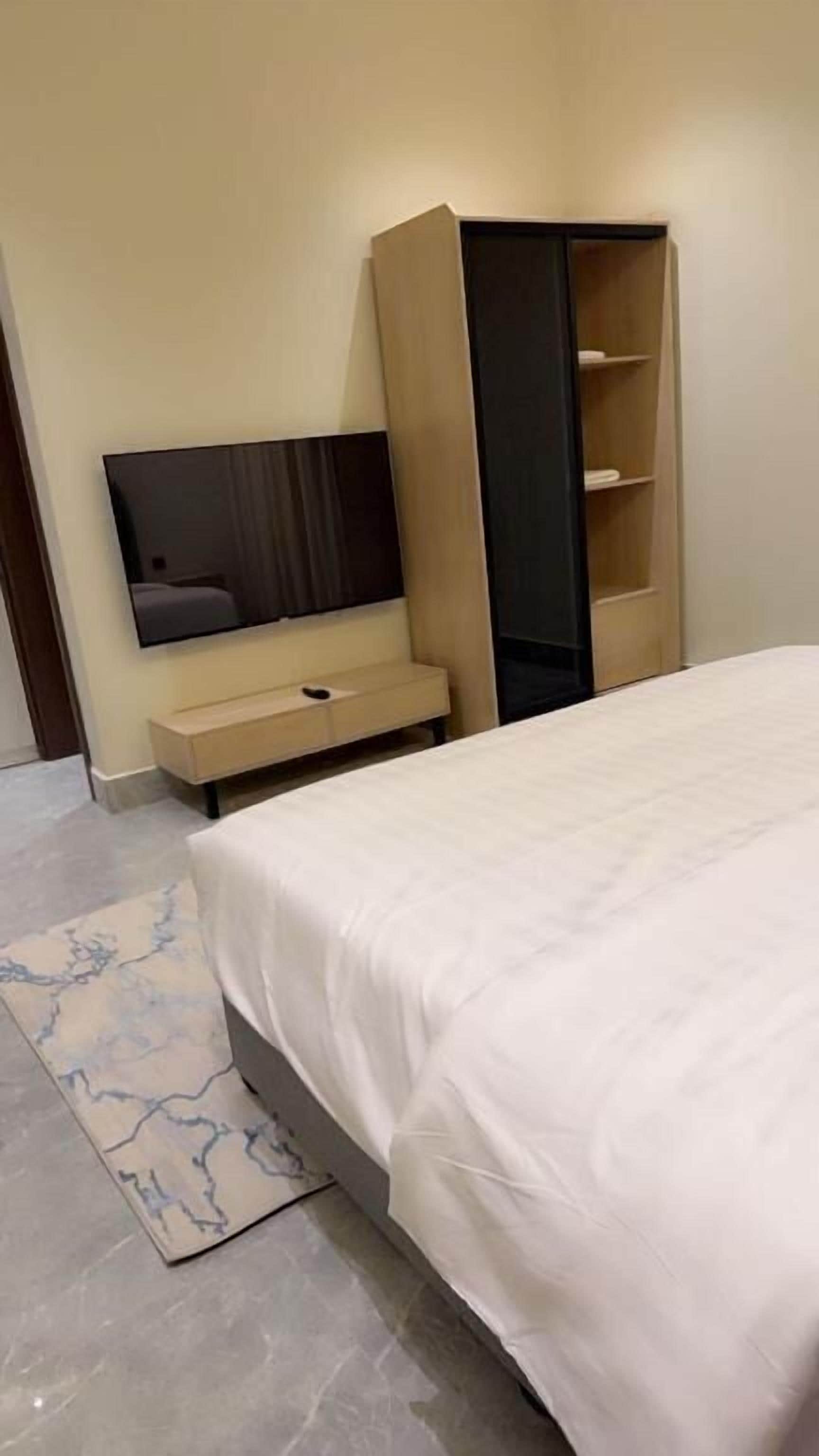 A bedroom with a bed, a TV, a wardrobe, and a small bench.