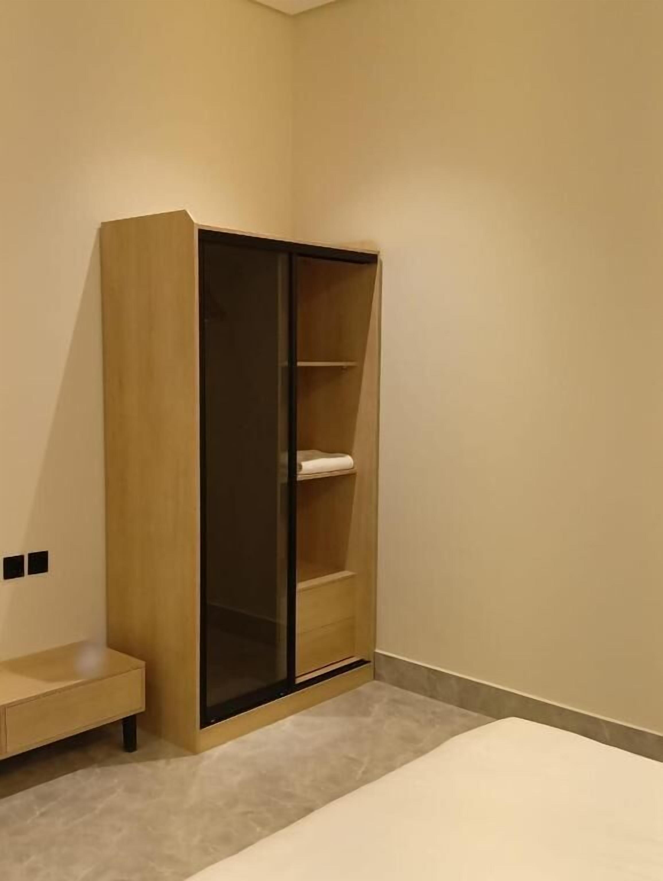 A room with a wooden wardrobe, a bed, and a small bench.