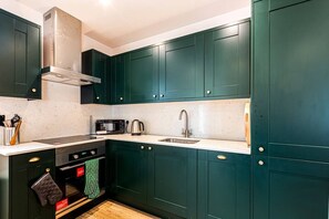A modern kitchen with dark green cabinets, a stainless steel range hood, a microwave, a kettle, and a sink. - Loft 1 - One bedroom house with parking (Nuneham Courtenay)