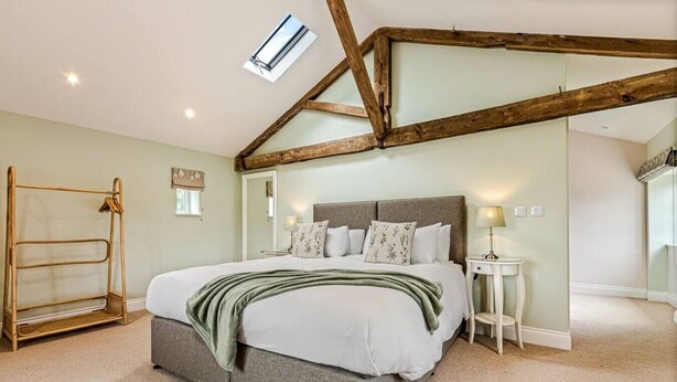 A bedroom with a bed, a bedside table, a lamp, a wardrobe, and a skylight.