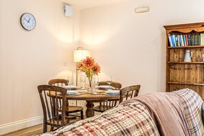 A dining area with a wooden table set for four, a clock on the wall, and a bookshelf filled with books. - Loft 1 - One bedroom house with parking (Nuneham Courtenay)