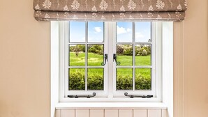A window with a white frame, a brown patterned valance, and a view of a green landscape.