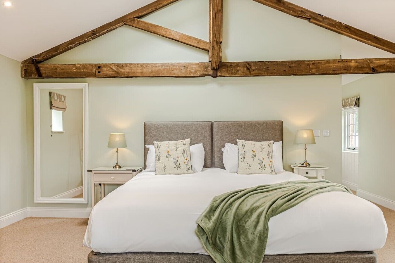 A bedroom with a large bed, two bedside tables with lamps, a mirror, and a window with curtains.