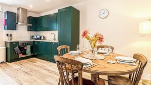 A kitchen with teal cabinets, a wooden dining table set for four, and a clock on the wall.
