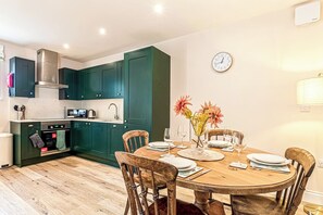 A kitchen with teal cabinets, a wooden dining table set for four, and a clock on the wall.