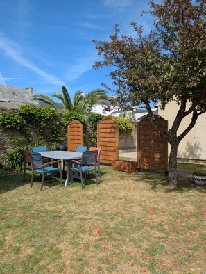 Une terrasse avec une table et des chaises, une clôture en bois et un arbre.