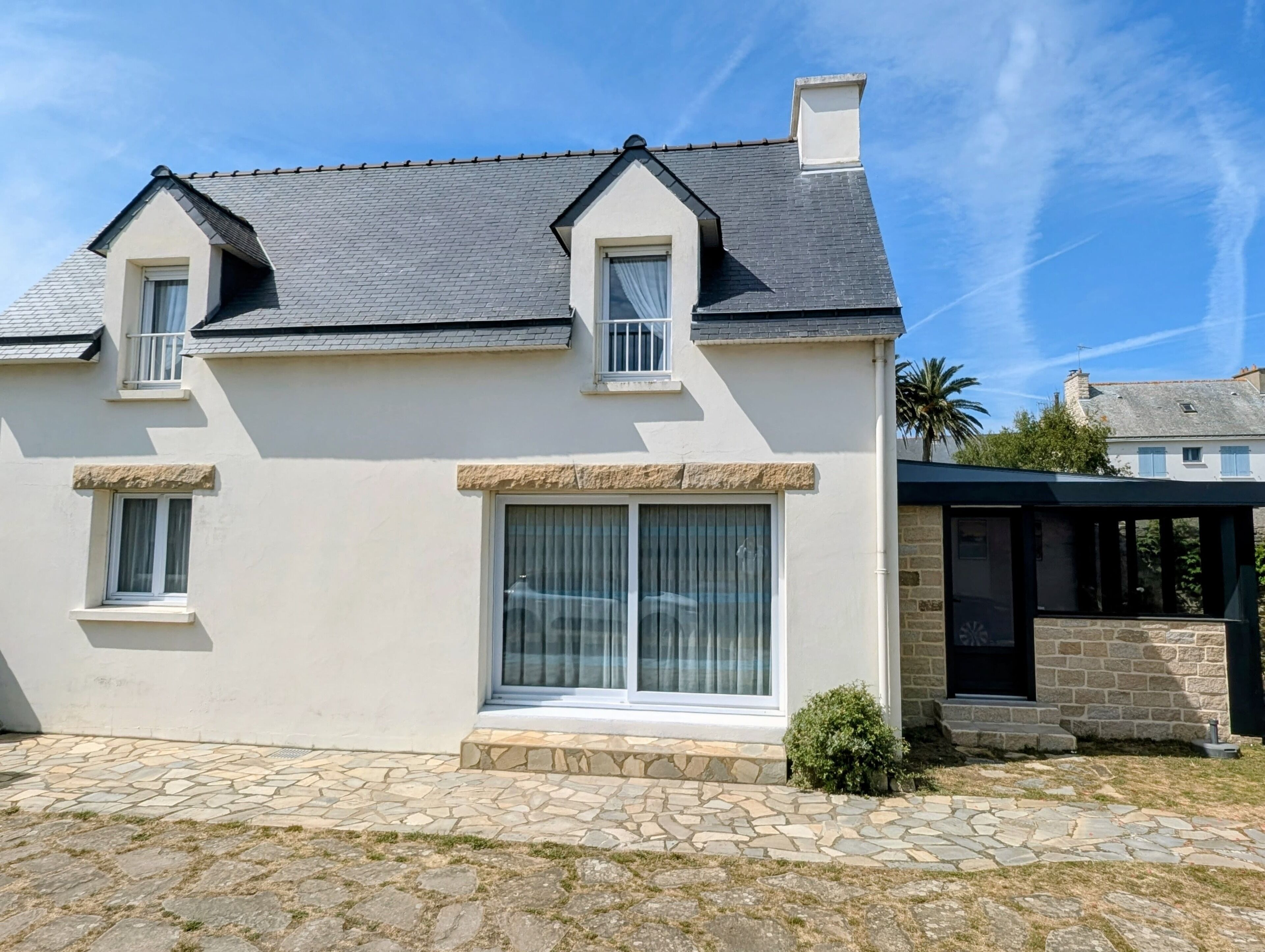 Une maison à deux étages, avec des fondations en pierre, une grande porte-fenêtre coulissante et un petit jardin.