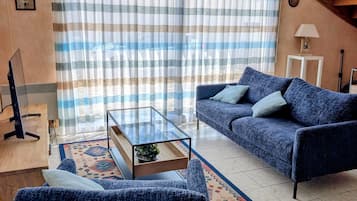 Un salon comprenant un canapé, un fauteuil, une table basse en verre et une lampe.