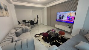 Ein modernes Wohnzimmer mit einem Ecksofa, einem Glastisch und einem wandmontierten Flachbildfernseher.
