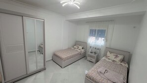 Une chambre avec deux lits simples, une armoire, une table de chevet et une fenêtre avec des rideaux.