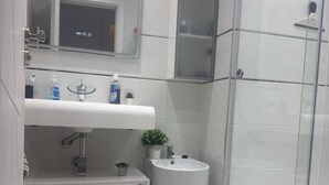 Ein Badezimmer mit Duschkabine aus Glas, einem weißen Waschbecken, einem Spiegel und einer Toilette.
