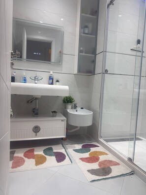 Une salle de bain avec une douche à parois de verre, un lavabo blanc, un miroir et des toilettes.