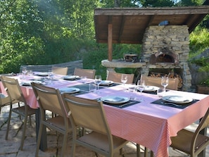 Un área de comedor al aire libre con un horno de piedra, mesas y sillas de madera.