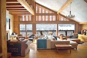 A spacious loft-style room with a high ceiling, large windows, and a balcony with a view of snow-covered trees. - Chalet Cannelle (La Chapelle-d'Abondance)