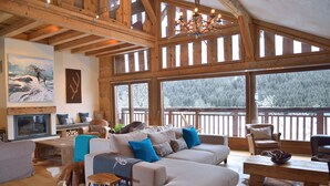 A cozy living room with a fireplace, large windows, and a wooden ceiling. - Chalet Cannelle (La Chapelle-d'Abondance)