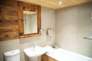 A bathroom with a wooden ceiling, a large mirror, a sink, a toilet, and a shower area.