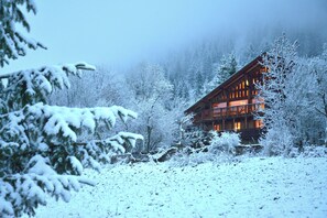 Uma cabana de madeira com várias janelas e varanda, rodeada por árvores cobertas de neve.