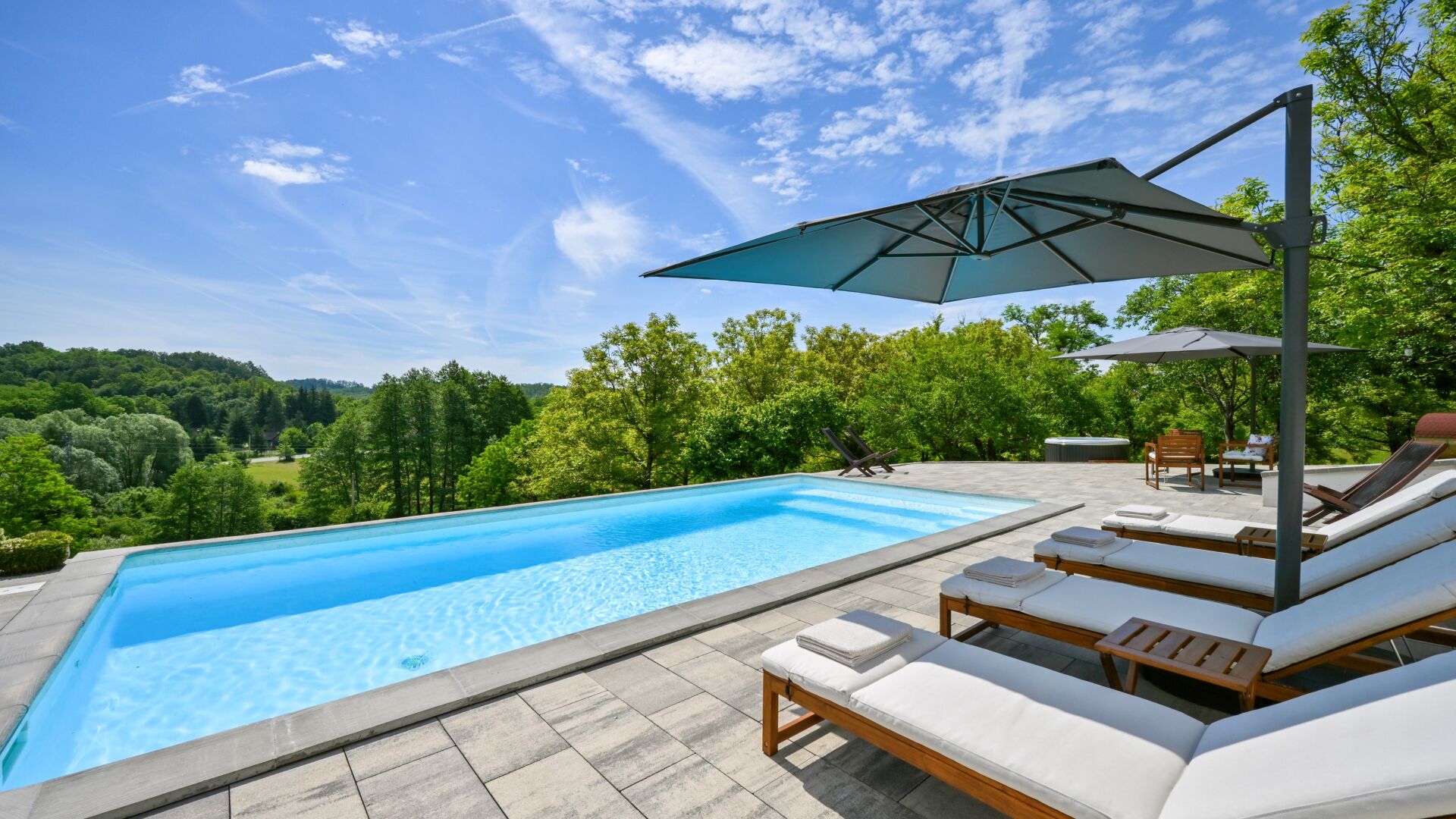 Ein Schwimmbecken mit Liegestühlen und Sonnenschirmen, umgeben von Bäumen und Blick auf die Landschaft.