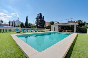 A rectangular swimming pool with a white deck, surrounded by green grass and a white fence. - Villa Can Benavent by Slow Villas (Arenal)