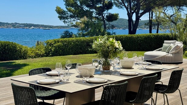 An outdoor dining area with a table set for four, surrounded by greenery and overlooking a body of water. - La Voile - Beachfront family villa - Pool Direct beach access Saint-Tropez 5 min (Grimaud)