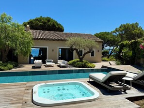 Ein Poolbereich mit Whirlpool, Liegestühlen und einem Gebäude mit einem Ziegeldach und offenen Türen.