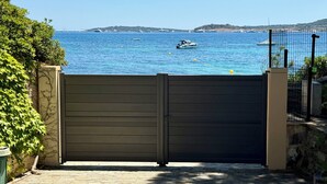 A view through a closed gate to a coastal area with boats on the water and a distant island. - La Voile - Beachfront family villa - Pool Direct beach access Saint-Tropez 5 min (Grimaud)