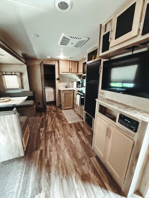 A compact RV kitchen with wooden cabinets, a black refrigerator, a microwave, and a built-in TV. - Cozy 1-bedroom Camper in lovely Gamaliel just 4 minutes from the LAKE (Gamaliel)