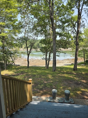 A wooden deck leading to a grassy area with trees and a body of water. - Bridges Camp - Private Beach! Dogs welcome! (Little Deer Isle)