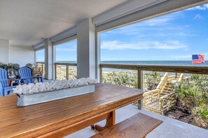 Eine hölzerne Bank mit einer weißen Blumenkomposition, blauen Stühlen und Blick auf den Strand mit einer amerikanischen Flagge.
