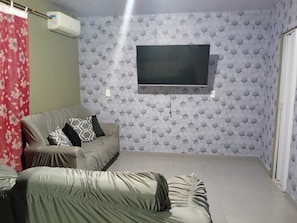 A room with a grey sofa, a TV mounted on the wall, and a patterned hexagonal wall design. - House on the big beach (São Francisco do Sul)