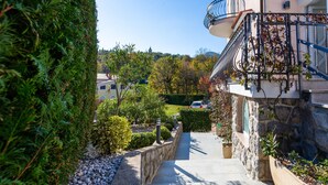 A residential building with a stone facade, a balcony with a wrought iron railing, and a pathway leading to a green lawn. - Apartman Mihaela with pool by Villas Guide (Kuceli)