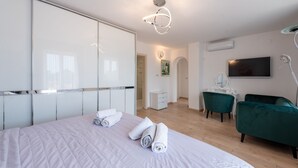 A hotel room with a bed, a vanity with a mirror, a green chair, and a flat-screen TV. - Apartman Mihaela with pool by Villas Guide (Kuceli)