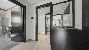 Una cocina moderna con un refrigerador negro grande, una zona de comedor con taburetes de bar y un pasillo que lleva a un baño.