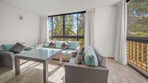 Una sala de estar moderna con una mesa de centro de vidrio, sofás de mimbre y un gran ventanal con cortinas.